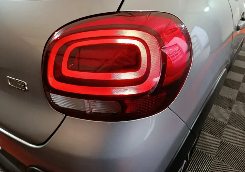 Gros plan sur le feu arrière droit rouge d'une Citroën C3 gris clair, avec logo C3 visible sur la carrosserie.
