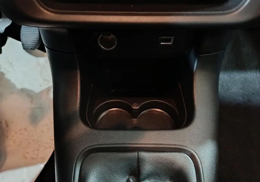 Vue rapprochée de la console centrale noire avec porte-gobelets, prise 12V et port USB sur Citroën C3 gris clair 2024.
