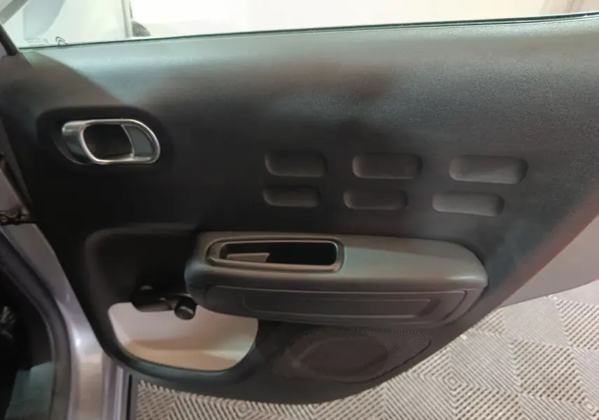 Vue intérieure côté gauche de la porte avant gris clair de la Citroën C3 avec poignée et haut-parleur intégrés.