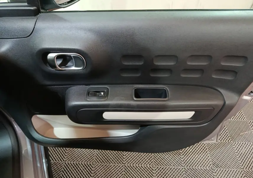 Vue rapprochée de la porte côté conducteur de la Citroën C3 gris clair, montrant la poignée intérieure et les commandes de fenêtre.