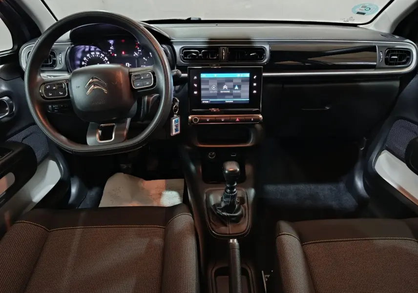 Vue intérieure avant de la Citroën C3 2024, tableau de bord noir avec écran tactile central et volant multifonctions.
