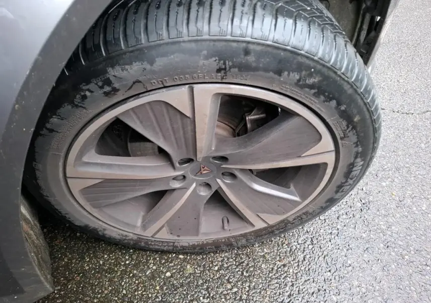 Gros plan sur la jante alu gris foncé avec logo CUPRA au centre, montée sur un pneu noir humide.