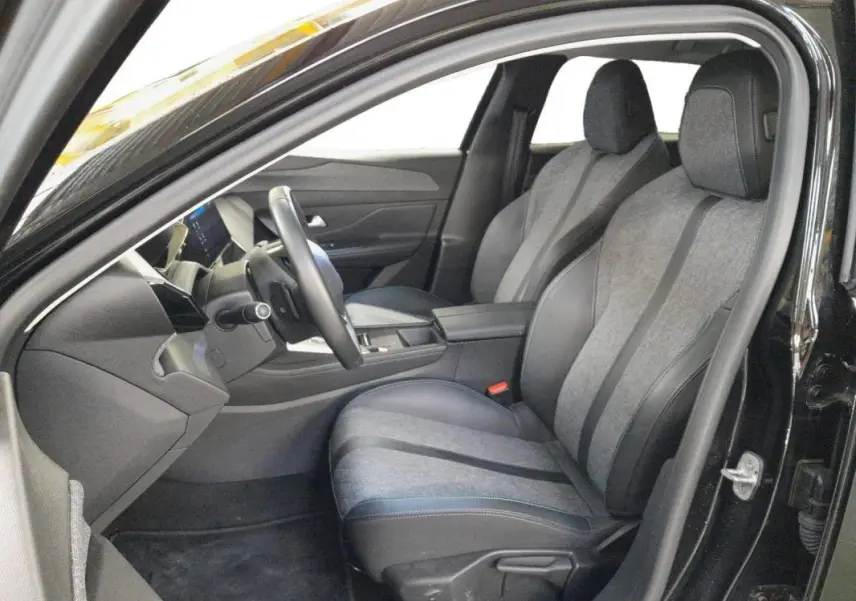 Vue intérieure côté conducteur de la Peugeot 408 PHEV 180 e-EAT8 Allure 2024 noire, sièges tissu et cuir gris.