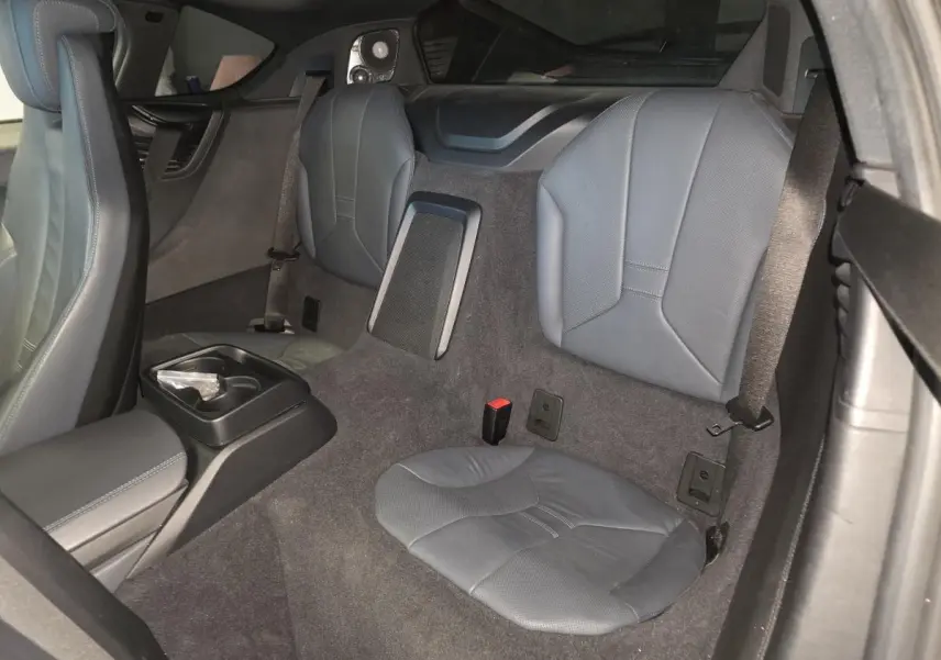 Vue intérieure arrière droite de la BMW i8 noire, montrant les sièges arrière en cuir perforé et la console centrale avec porte-gobelets.