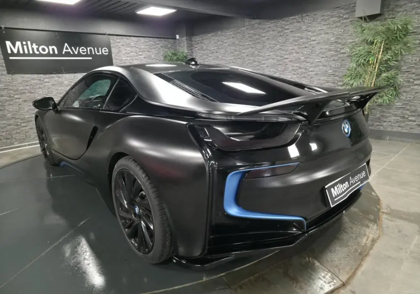 BMW i8 Coupé Pure Impulse noir mat vue 3/4 arrière droit avec aileron carbone et détails bleus lumineux.