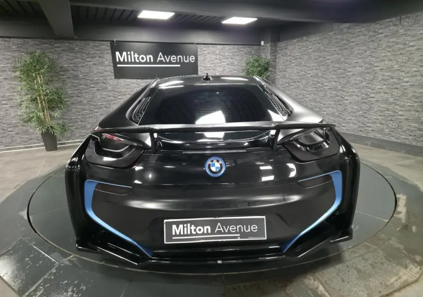 Vue arrière d'une BMW i8 Coupé Pure Impulse noir mat avec détails bleus et aileron carbone en intérieur showroom.