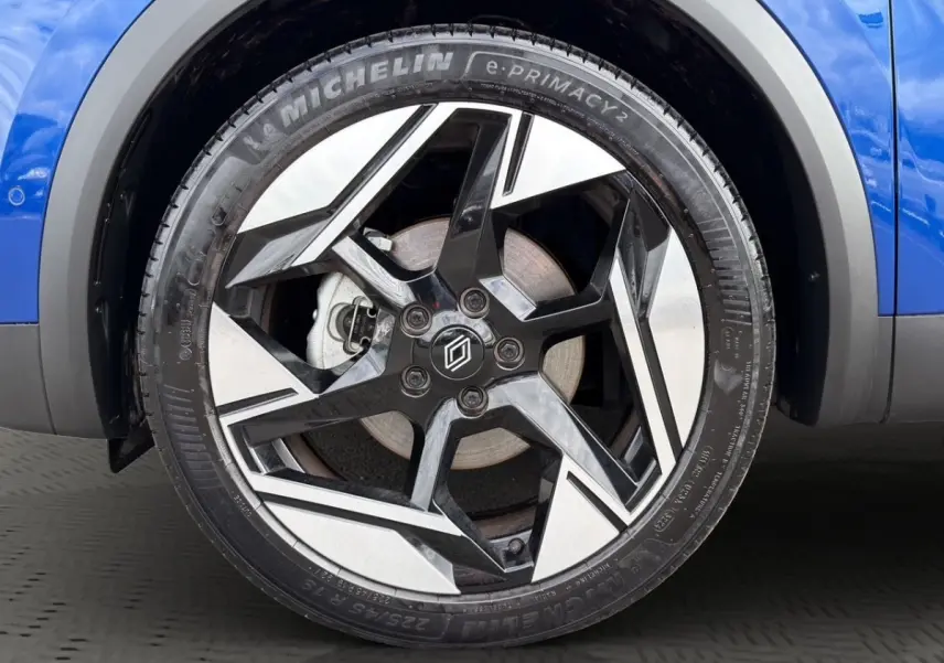 Gros plan sur la roue avant droite bleu Renault Symbioz avec jante noire et argentée au design géométrique.