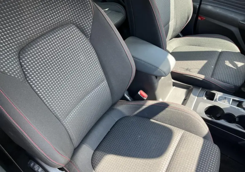 Gros plan sur les sièges avant noirs avec surpiqûres rouges et accoudoir central dans l’habitacle d’une Ford Focus SW bleue.