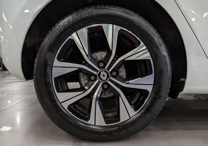 Gros plan sur la roue avant droite d’une Renault Clio V blanc glacier, jante alliage bicolore au design moderne.