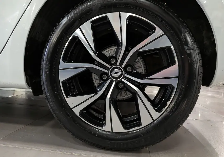 Gros plan sur la roue avant droite d’une Renault Clio V blanche, jante alliage bicolore avec logo Renault central.