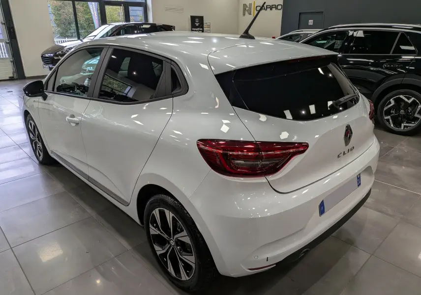 Renault Clio V blanc Glacier vue 3/4 arrière droit en intérieur, avec vitres teintées et jantes alliage noires.
