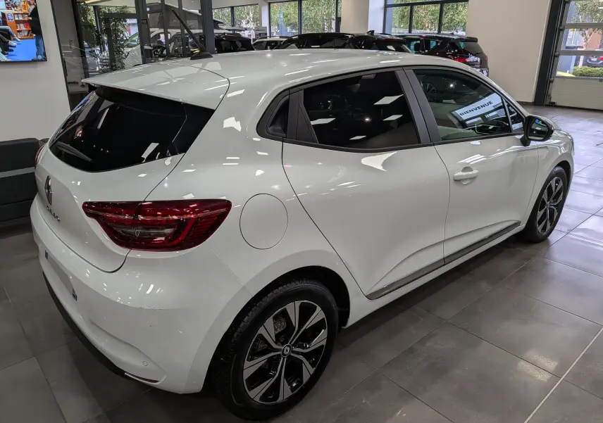 Renault Clio V blanc glacier vue 3/4 arrière droit en intérieur, avec jantes alliage et vitres teintées.