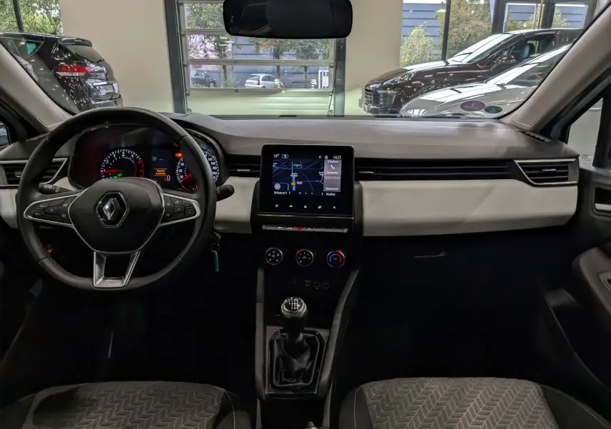 Vue intérieure avant de la Renault Clio V blanche, tableau de bord avec écran tactile et volant multifonction.