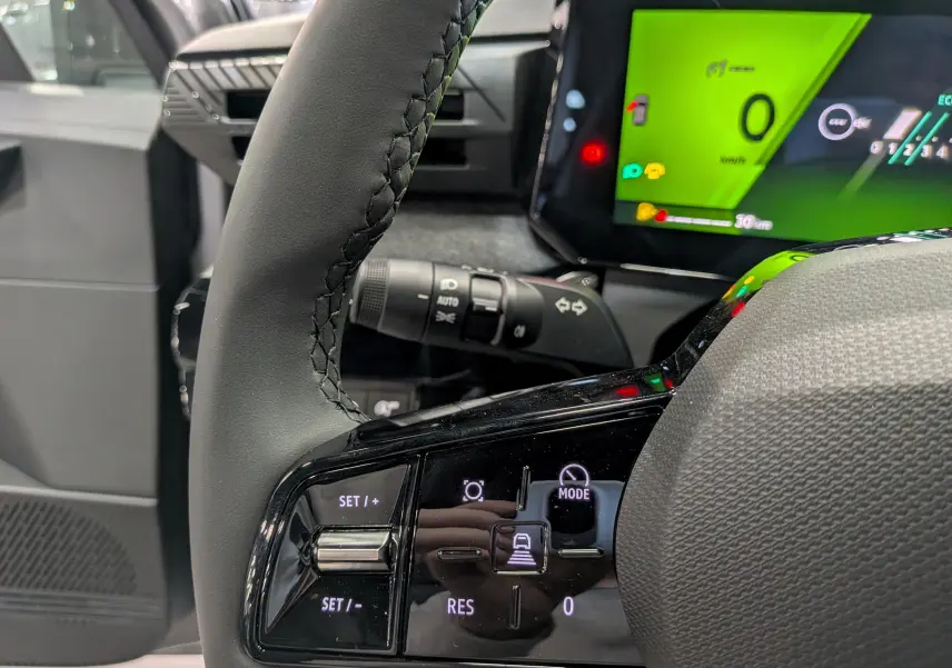 Gros plan sur le volant et la commande de régulateur de vitesse d'une Renault Clio VI gris schiste, avec tableau de bord numérique vert.