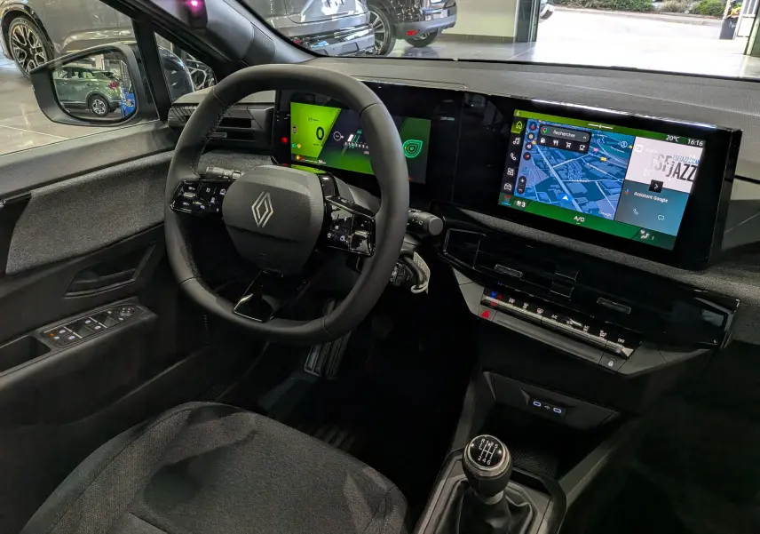 Vue intérieure côté conducteur de la Renault Clio VI gris schiste, avec tableau de bord numérique et écran tactile central.