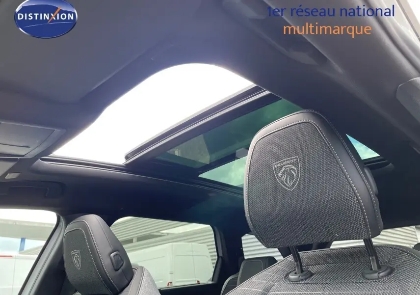 Vue intérieure du Peugeot 5008 Hybrid 2025 montrant les sièges avant en cuir noir avec logo Peugeot et toit panoramique ouvert.