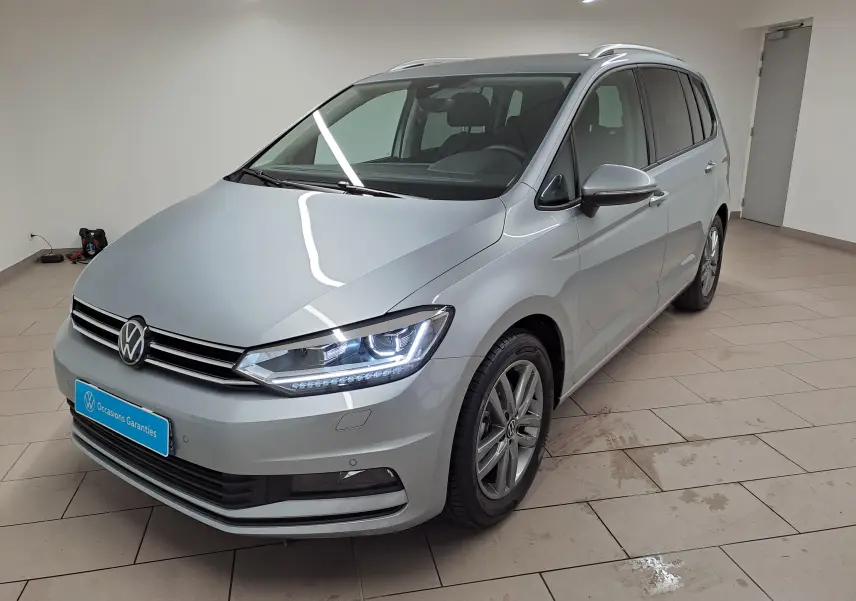 Volkswagen Touran 2025 argent Dolomite en 3/4 avant droit, avec feux LED et jantes alliage visibles.