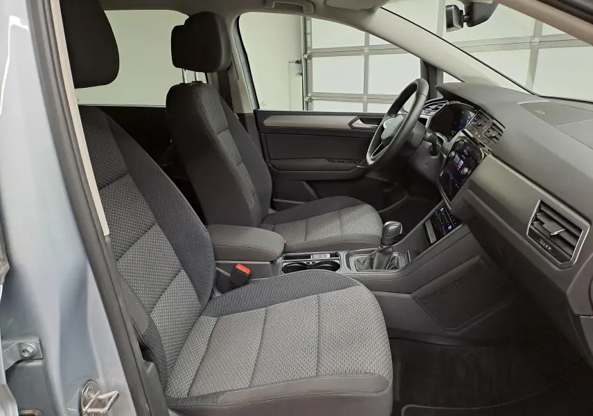 Intérieur avant du Volkswagen Touran 2025, vue côté gauche, sièges tissu gris et tableau de bord moderne.