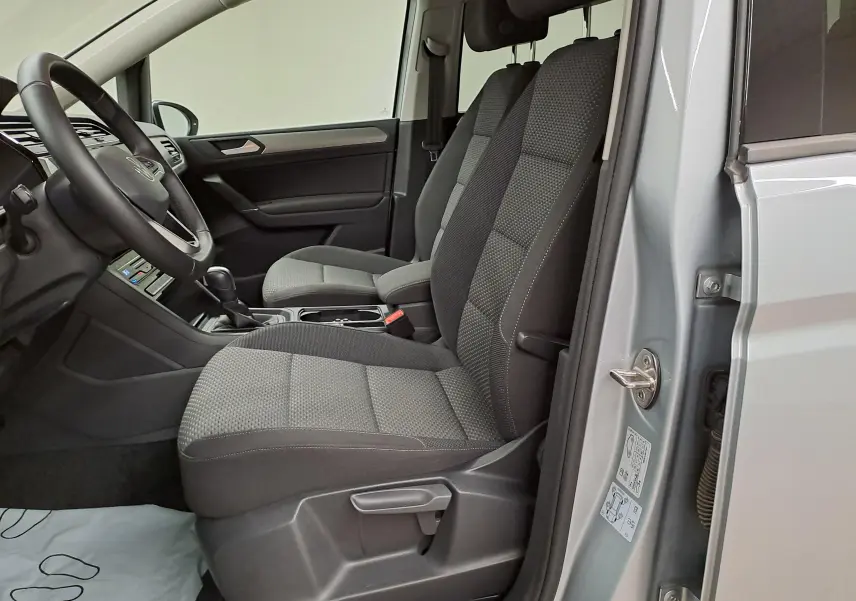 Vue intérieure côté conducteur du Volkswagen Touran 2025 argent Dolomite, montrant les sièges avant en tissu gris.