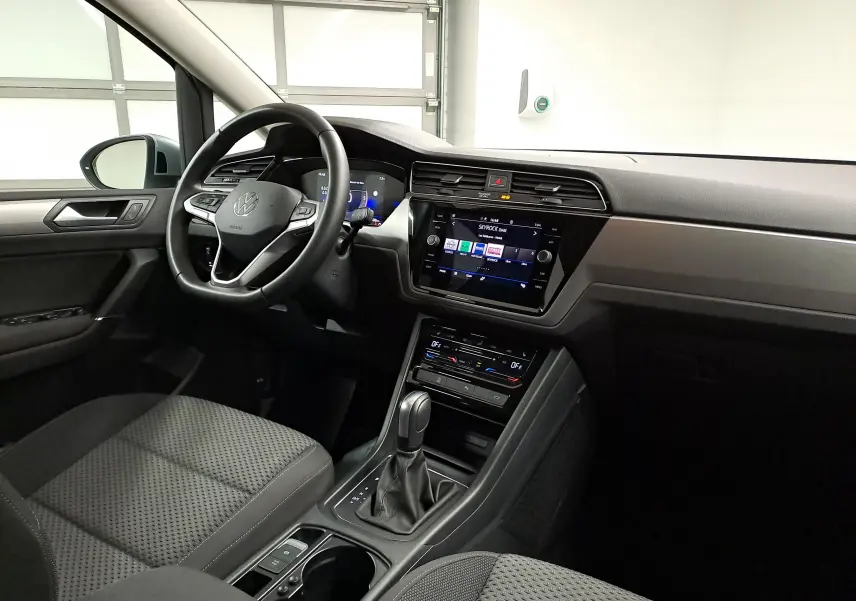 Vue intérieure côté conducteur du Volkswagen Touran 2025, tableau de bord moderne avec écran tactile et volant multifonction noir.