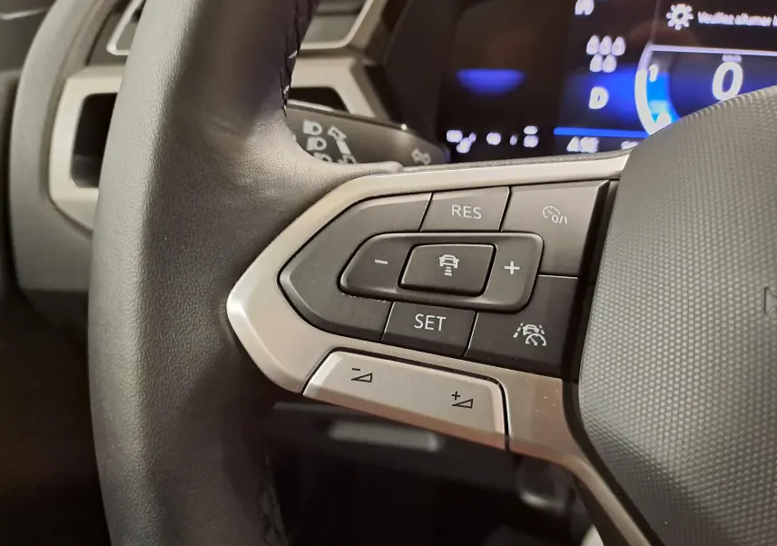 Gros plan sur les commandes au volant côté gauche du Volkswagen Touran 2025, avec affichage numérique en arrière-plan.