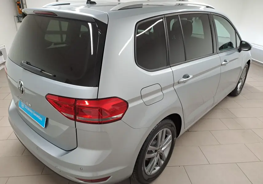 Vue 3/4 arrière droit du Volkswagen Touran 2025 en Argent Dolomite métallisé avec vitres teintées et jantes alliage.