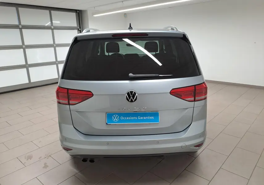 Vue arrière du Volkswagen Touran 2025 en argent Dolomite, avec feux rouges et logo VW bien visibles dans un garage.