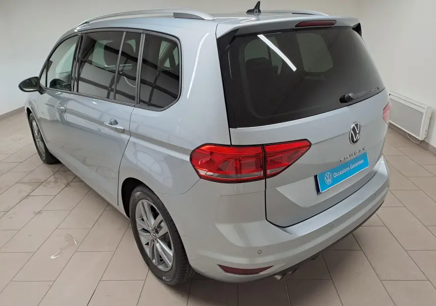 Vue 3/4 arrière droite d'un Volkswagen Touran 2025 argent Dolomite avec vitres teintées et jantes alliage.
