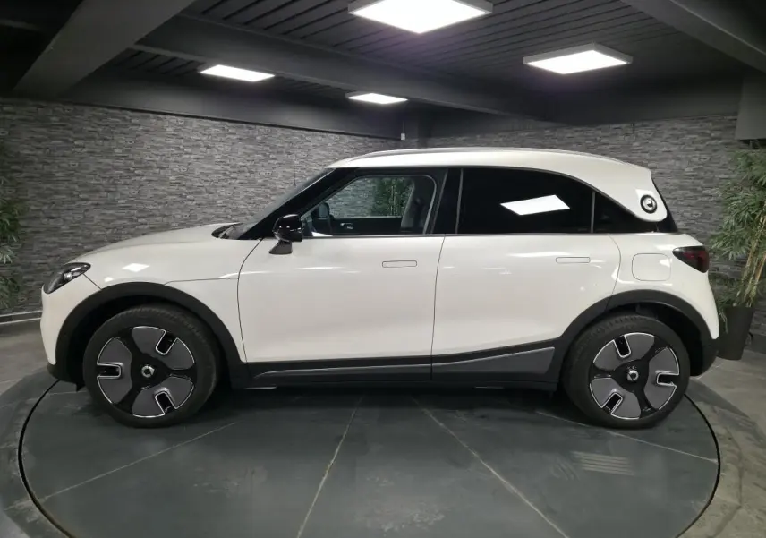 Vue latérale droite d'une Smart #1 électrique blanche avec jantes design et toit contrasté noir en intérieur showroom.