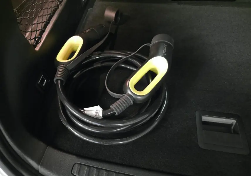 Câble de recharge électrique noir avec poignées jaunes dans le coffre d'une Smart Electric blanche, vue intérieure.