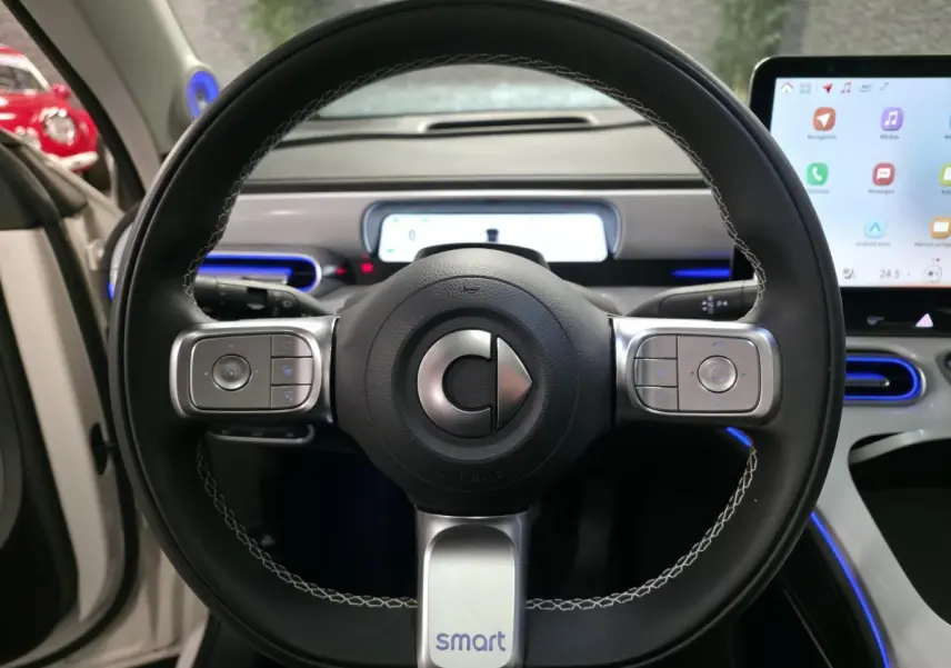 Volant cuir noir avec surpiqûres blanches de la Smart Electric Premium 2024, tableau de bord et écran tactile en arrière-plan.