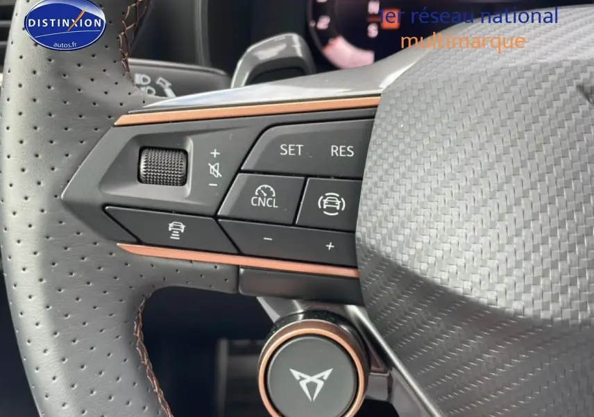 Gros plan sur le volant cuir perforé avec commandes multifonctions et logo CUPRA au centre, intérieur noir et cuivre.