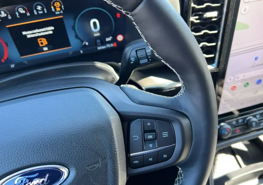 Gros plan sur le volant cuir noir avec commandes multifonctions du Ford Ranger 2026, tableau de bord numérique en arrière-plan.