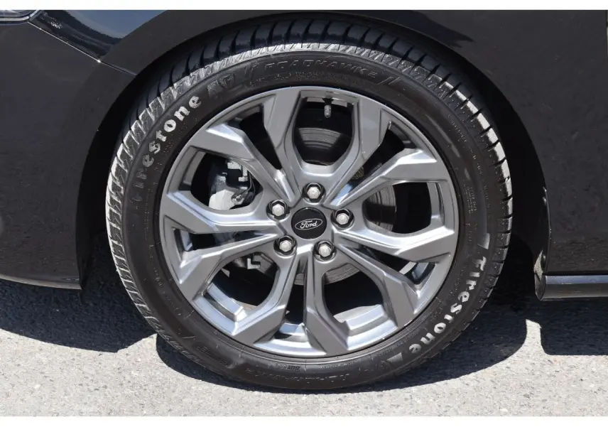 Gros plan sur la roue avant gauche de la Ford Focus SW 2025 Agate Black avec jante alliage grise et pneu Firestone.