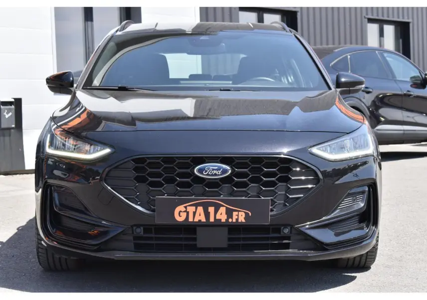 Vue avant d'une Ford Focus SW 2025 Agate Black Metallic avec calandre hexagonale et phares LED allumés.