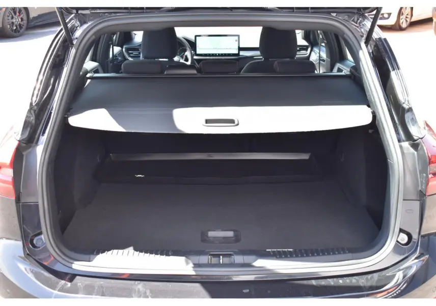 Vue arrière du coffre ouvert de la Ford Focus SW Agate Black Metallic, intérieur noir avec tablette cache-bagages déployée.