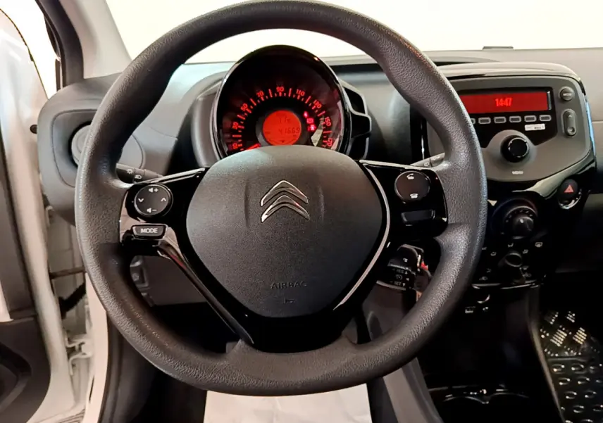 Vue rapprochée du volant noir de la Citroën C1 blanc, avec tableau de bord et console centrale visibles en arrière-plan.