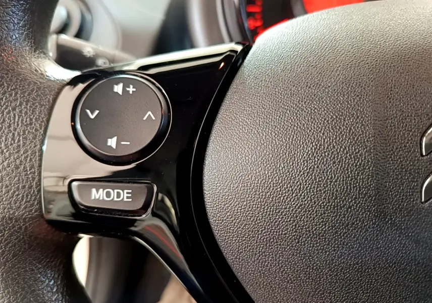 Gros plan sur les commandes noires du volant de la Citroën C1 blanche, mettant en avant les boutons de volume et mode.