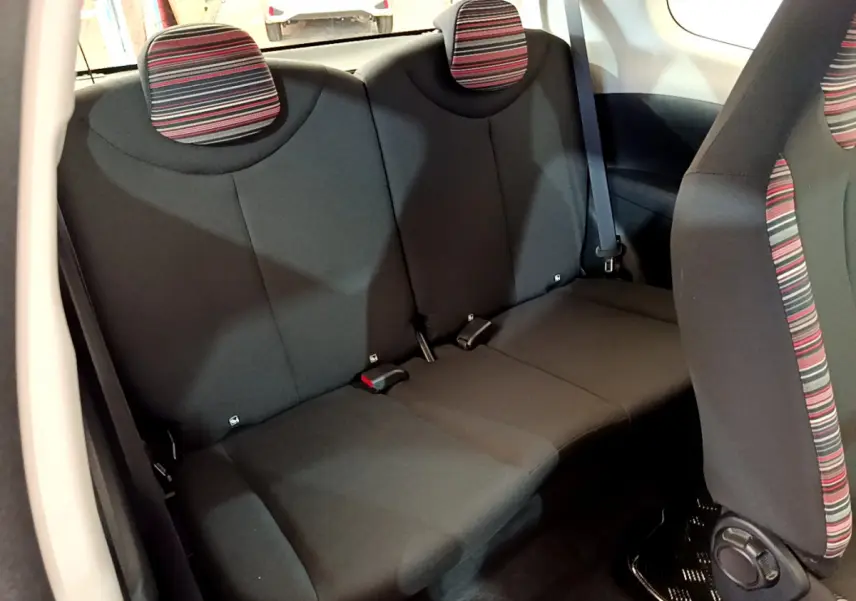 Vue intérieure arrière de la banquette noire avec appuie-têtes rayés rouges et gris de la Citroën C1 blanche.