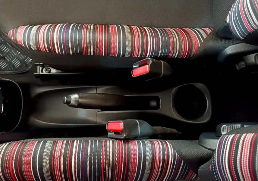 Vue plongeante sur la console centrale de la Citroën C1 blanche, avec frein à main et sièges rayés rouges, noirs et blancs.