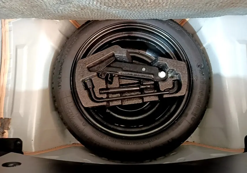 Vue rapprochée de la roue de secours noire avec outils de bord dans le coffre blanc d’une Citroën C1 blanche.