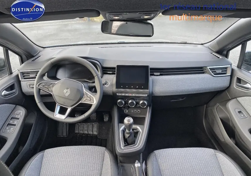 Vue intérieure avant de la Renault Clio V gris rafale, volant multifonction, écran tactile et levier de vitesse manuel visibles.