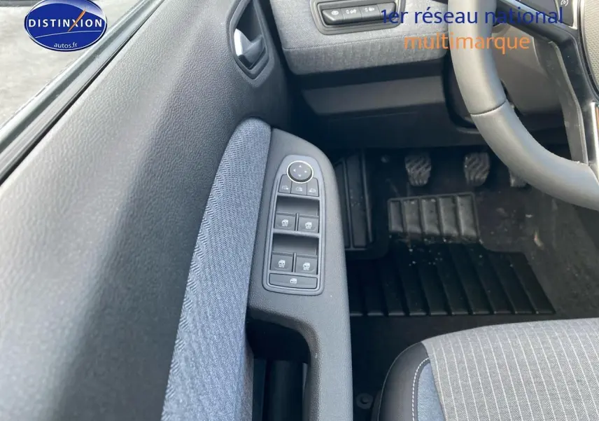 Vue intérieure côté conducteur de la Renault Clio V gris rafale, montrant les commandes des vitres et le pédalier.