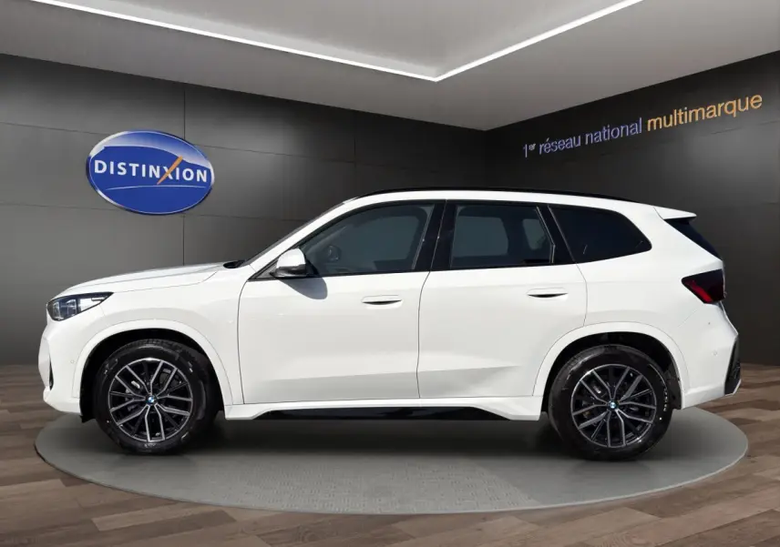 BMW X1 sDrive20d blanc vue de profil côté gauche avec jantes noires en showroom intérieur