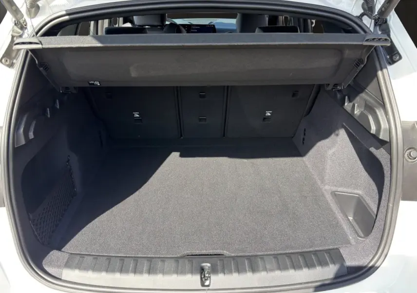 Coffre ouvert vu de l'arrière d'un BMW X1 blanc 2025, espace de chargement propre et spacieux avec cache-bagages.