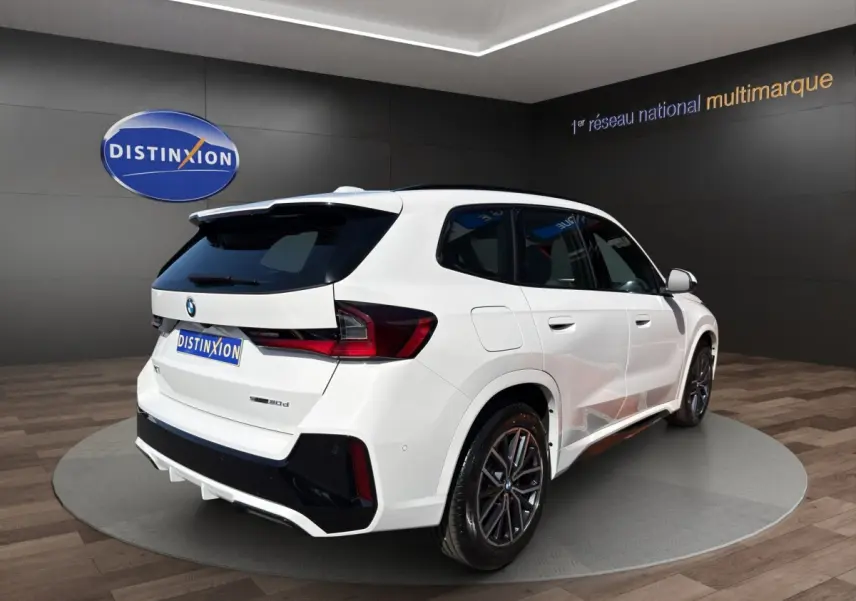 BMW X1 sDrive20d blanc en 3/4 arrière droit avec toit noir et jantes sport dans showroom
