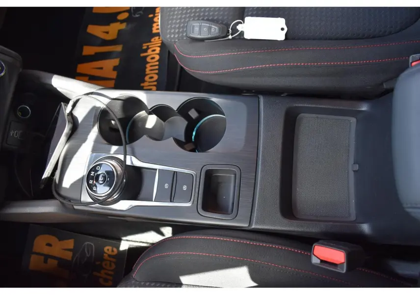 Vue plongeante sur la console centrale de la Ford Focus SW Moondust Silver, avec sélecteur rotatif de boîte auto et sièges noirs à surpiqûres rouges.