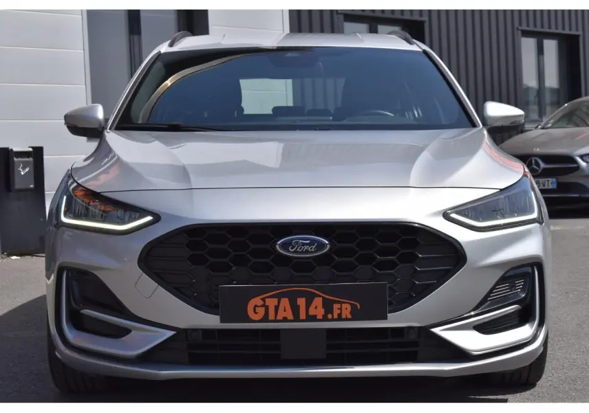 Vue frontale d'une Ford Focus SW 1.5 EcoBlue 115 ST LINE X en Moondust Silver avec calandre noire et feux LED allumés.