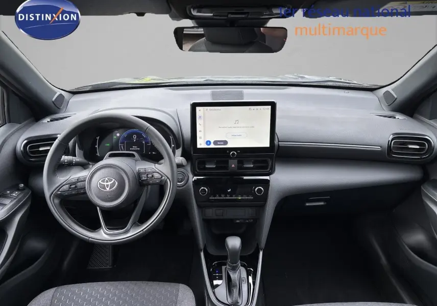 Vue intérieure avant de la Toyota Yaris Cross 1.5 Hybrid, tableau de bord noir avec écran tactile central et volant multifonction.