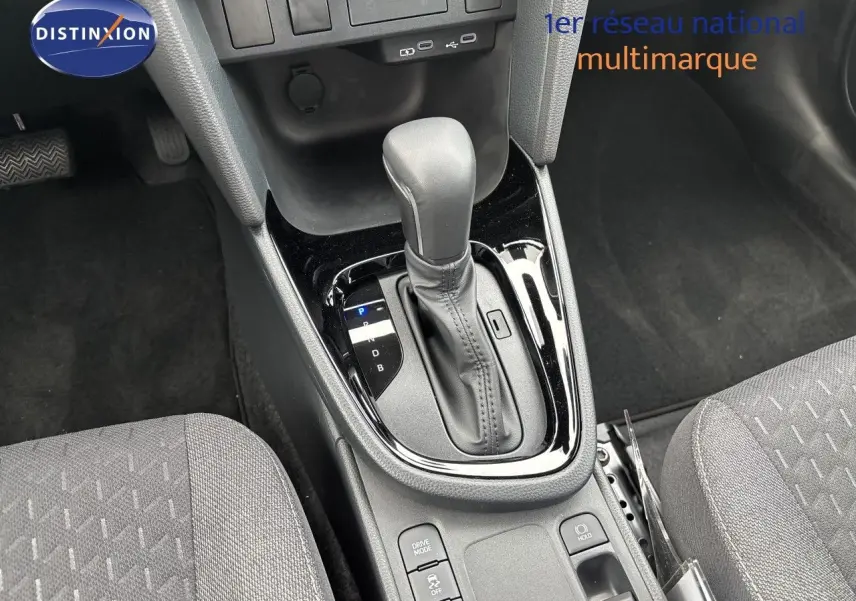 Gros plan sur la console centrale de la Toyota Yaris Cross hybride, mettant en valeur le levier de vitesse automatique et les sièges tissu gris.